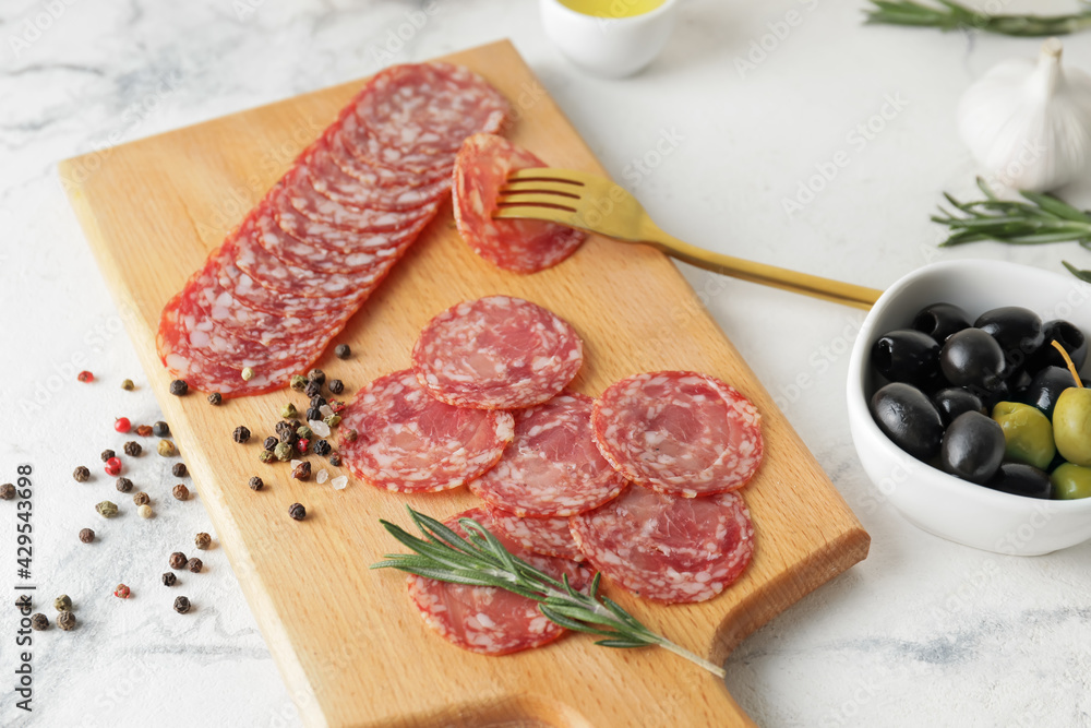 Board with tasty salami on light background