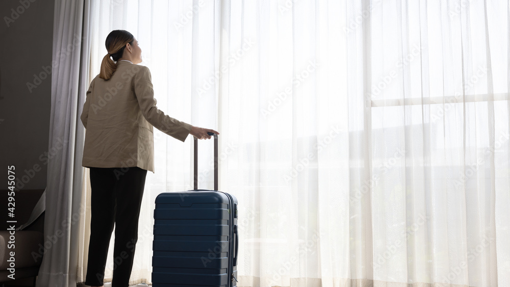 Young Asian girl in smart casual dress takes a breath moment at an apartment room window to inspire relax and stretch. Female visitor or traveler stands in front of white curtain look out for future. Young Asian girl in smart casual dress takes a breath moment at an apartment room window to inspire relax and stretch. Female visitor or traveler stands in front of white curtain look out for future.