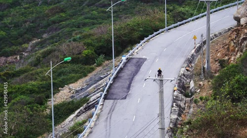 Tracking shot driving up a curvy road on motorbike carrying kite surfing board, watersports session trip