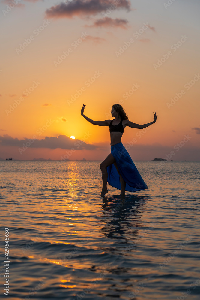 Young beauty girl dancing at tropical beach on sea water at paradise island at sunset. Summer concept