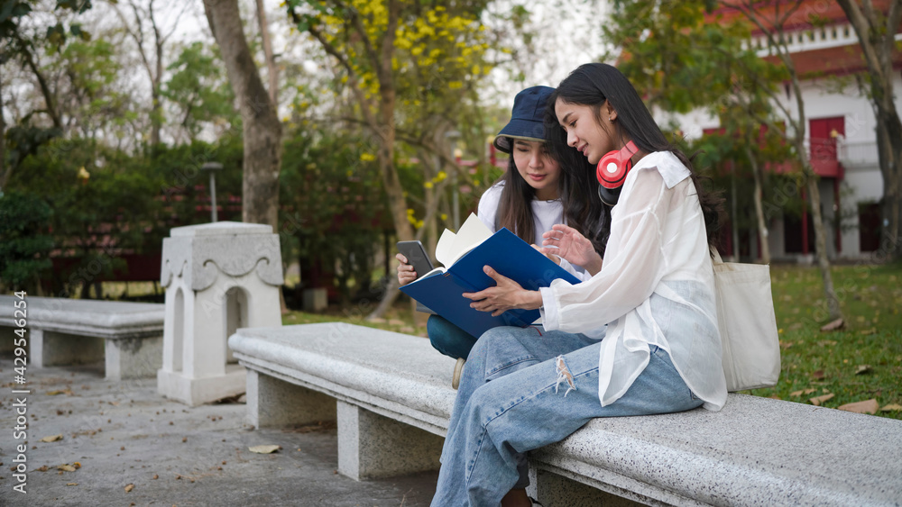 Two student sitting and reading book in park at the campus.