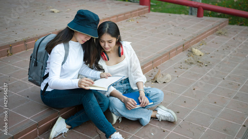 Two asian students sharing notes while sitting on staircase in the university campus.