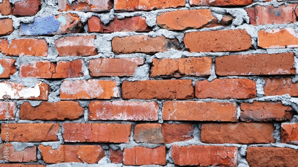 Obraz premium fragment of an old destroyed wall made of orange chipped bricks and abundant dried mortar, antique wall of an abandoned building, background of aged brickwork