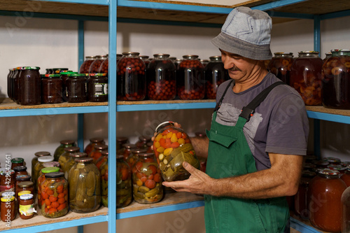 Man satisfied with the result of his work. He watches the shelves with marinated veggies in glass jares. Fermented organic food. photo