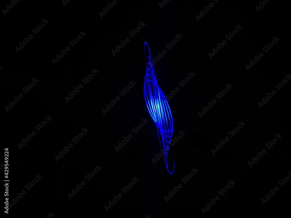 Obraz premium Closeup of Neon blue Spirograph geometric abstract pattern flowing in a isolated black background . Made using Long exposure technique, Light painting. Pendulum pattern.