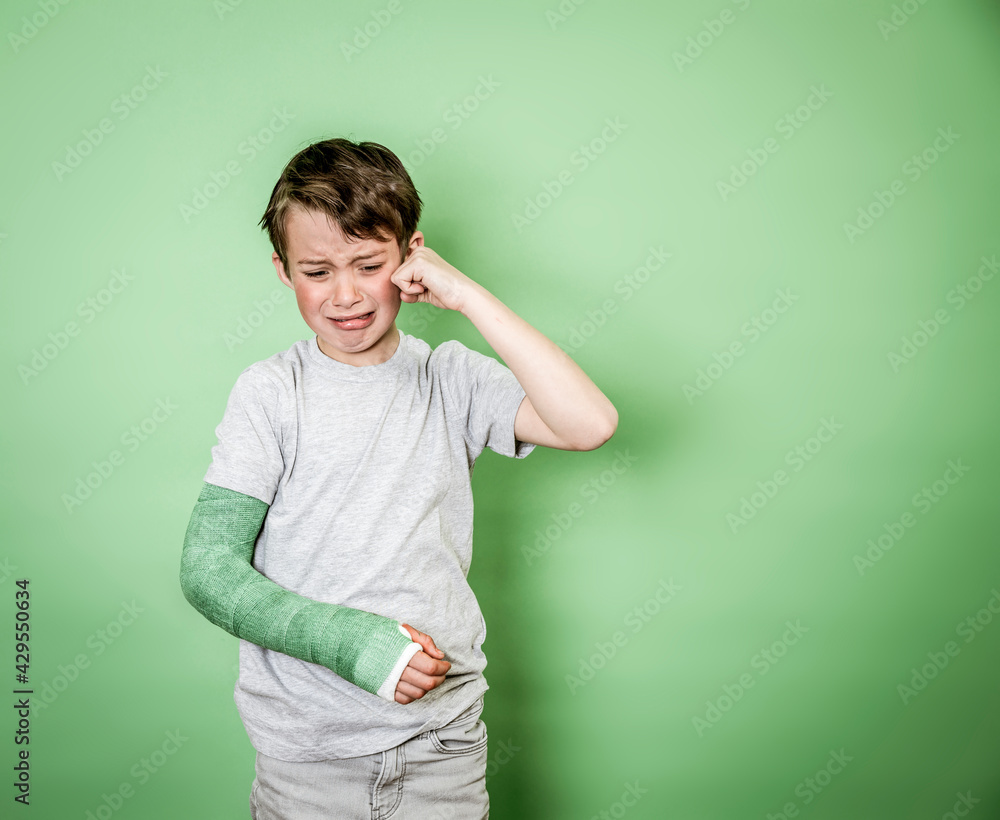 cool young schoolboy with broken arm and green arm plaster posing in front of green background cool young schoolboy with broken arm and green arm plaster posing in front of green background
