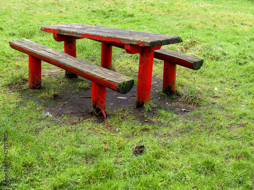 Old style red color wooden table and two benches in a park. Worn out surface.