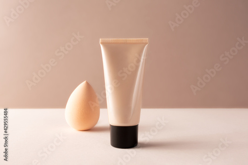 Tube tonal foundation makeup mockup and cosmetic beauty blender sponge on beige. BB or CC cream container for branding