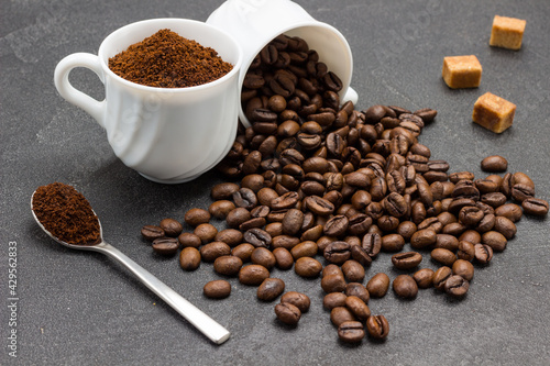 Ground coffee in cup and spoon. Roasted coffee beans are scattered from cup onto table