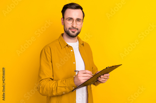Photo of smart confident young gentleman dressed casual outfit spectacles writing clipboard isolated yellow color background