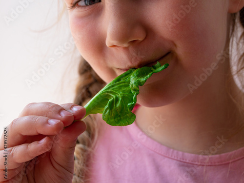 Little girl with fresh spinach in hand white background. Child eats natural raw clean food. Leaf vegetables vitamin Organic vegetarian meal superfood, nutritious smoothie salad vegan healthy lifestyle