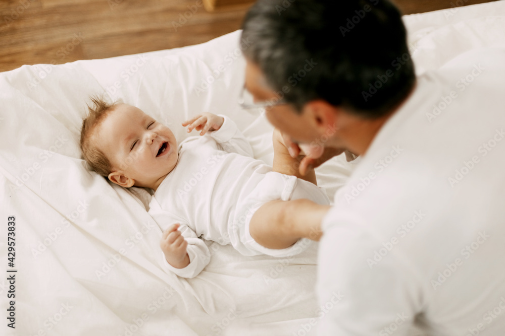 Happy father playing with adorable baby in the bedroom in a snow-white bed Happy father playing with adorable baby in the bedroom in a snow-white bed