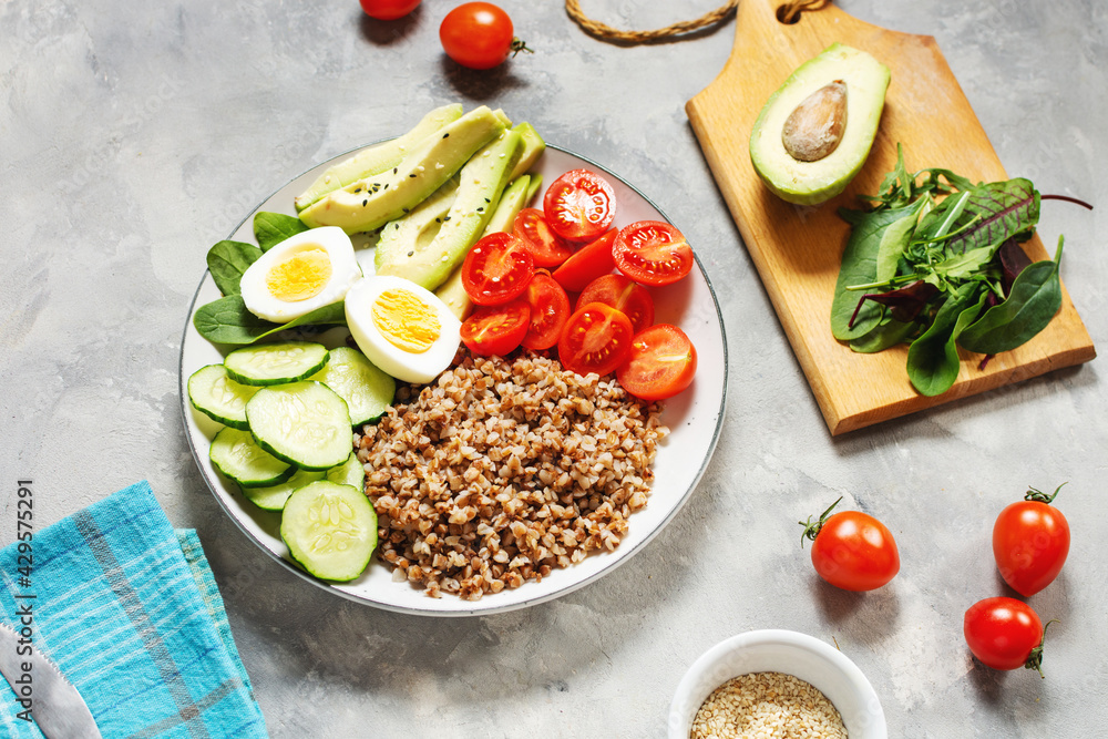 Vegan lunch bowl with avocado, egg, cucumber, tomato and buckwheat on concrete background Vegan lunch bowl with avocado, egg, cucumber, tomato and buckwheat on concrete background