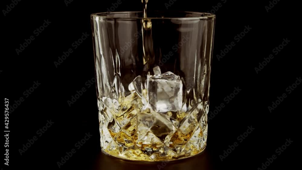 Slow Motion Shot of Pouring Whiskey into Glass. Alcohol pouring in the glass from the bottle. Slow Motion Shot of Pouring Whiskey into Glass. Alcohol pouring in the glass from the bottle.
