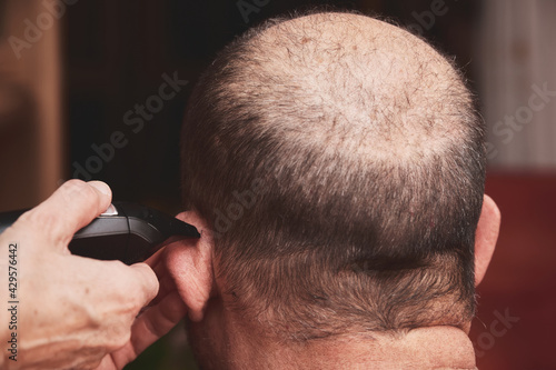 Wife cutting husbands hair at home with a haircut machine or hair clipper. © Ladanifer