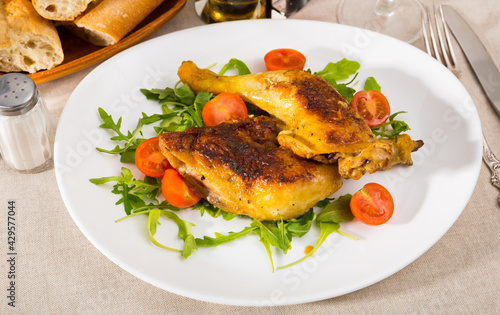 Plate of tasty snack roasted chicken legs with arugula and cherry tomatoes