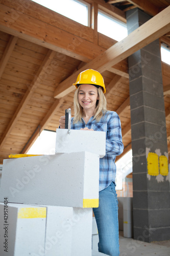 pretty young female bricklayer with yellow safety helmet is sawing bricks on a construction site in the house, concept female workers photo