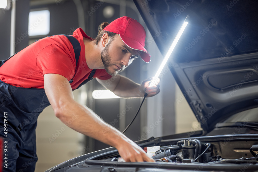 Auto mechanic with lamp checking car anatomy Auto mechanic with lamp checking car anatomy