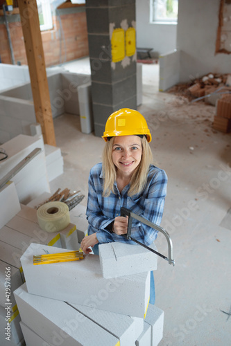 pretty young female bricklayer with yellow safety helmet is sawing bricks on a construction site in the house, concept female workers photo