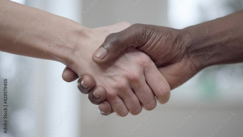 Close-up handshake of female Caucasian and male African American hands. Unrecognizable interracial couple holding hands indoors. International relationship and unity concept Close-up handshake of female Caucasian and male African American hands. Unrecognizable interracial couple holding hands indoors. International relationship and unity concept