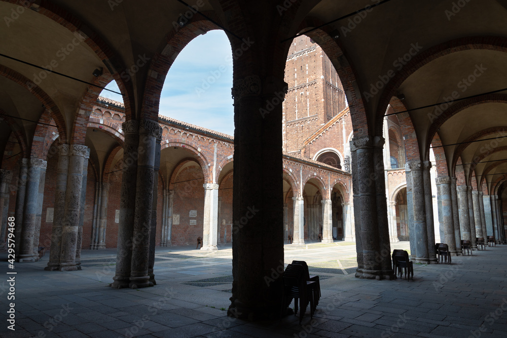 Silhouette of symmetrical arcades in the patio of the famous Sant'Ambrogio (meaning Saint Ambrogio) romanic cathedral in Milan, Italy. Blue sky in the background.