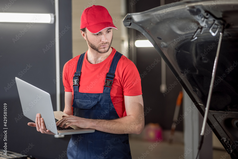 Auto mechanic with laptop looking under car hood Auto mechanic with laptop looking under car hood