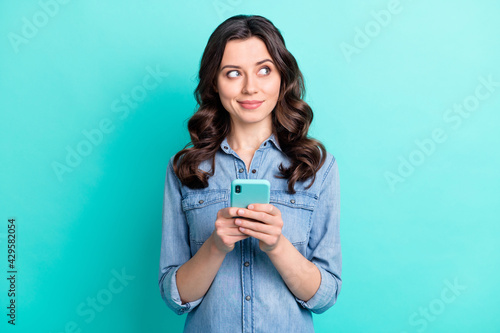Photo of young girl happy positive smile dream look empty space use smartphone isolated over turquoise color background