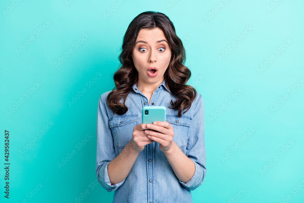 Photo of young girl amazed shocked look read browse fake news cellphone isolated over turquoise color background Photo of young girl amazed shocked look read browse fake news cellphone isolated over turquoise color background