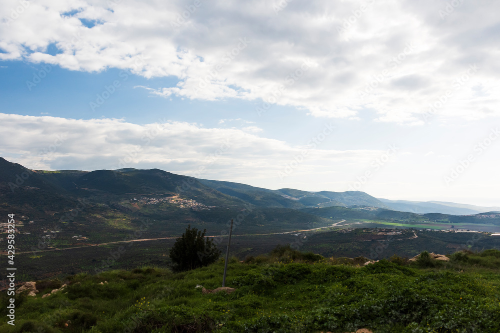 A view of a mountain range and a green valley in the morning at sunrise, against a dramatic backdrop of blue skies and clouds. North District Israel. High quality photo. Travel concept hiking