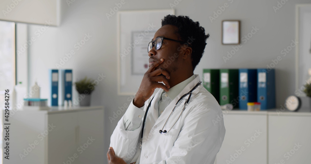 Thoughtful afro-american confident doctor standing in office looking away Thoughtful afro-american confident doctor standing in office looking away