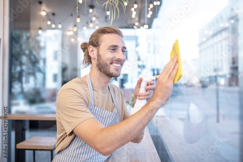 Smiling man wiping window in cafe in afternoon