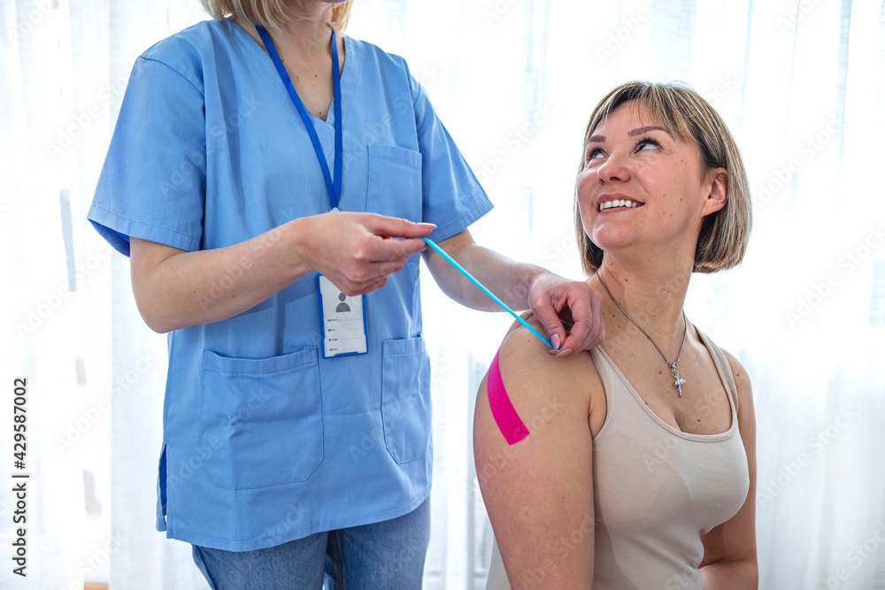 Kinesiotaping. Physical therapist applying tape to patient shoulder. Kinesiology taping treatment with blue and pink tape on athlete patient injured arm. Kinesiotaping. Physical therapist applying tape to patient shoulder. Kinesiology taping treatment with blue and pink tape on athlete patient injured arm.