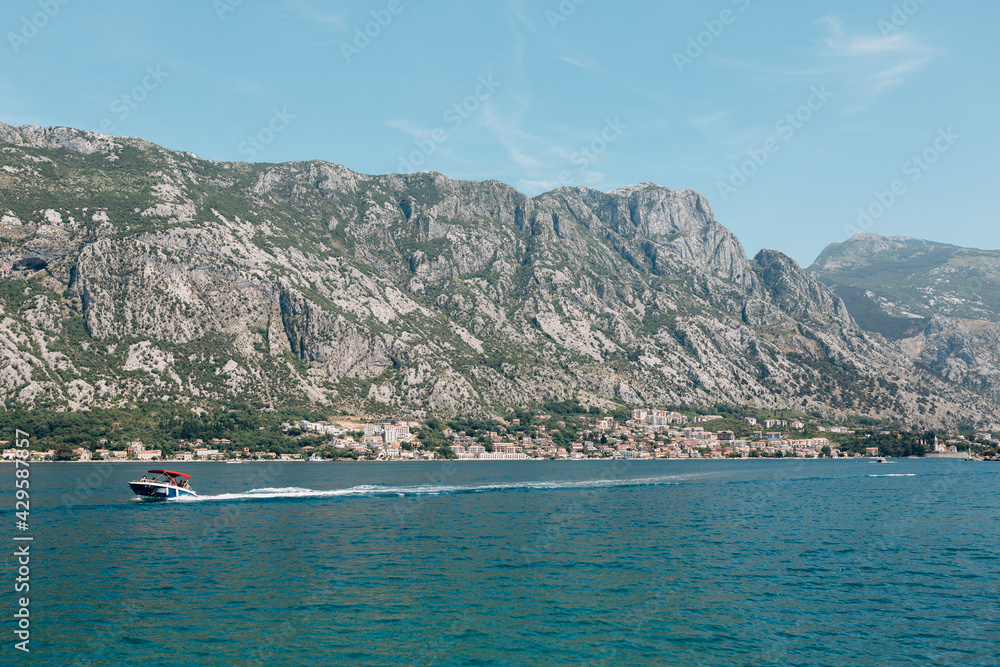 Motor boat with tourists on board sails along the Kotor bay against the backdrop of mountains 