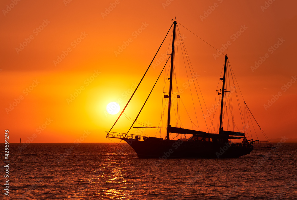 Close view of silhouette of sailing boat with sails down against sun at sunset, sun glare on sea waters. Romantic seascape