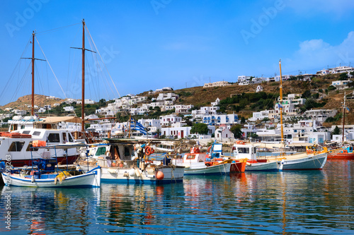 Beautiful summer day in typical marina of Greek island Mykonos, Greece. Colorful fishing boats moored at jetty. Mediterranean lifestyle, vacations. 