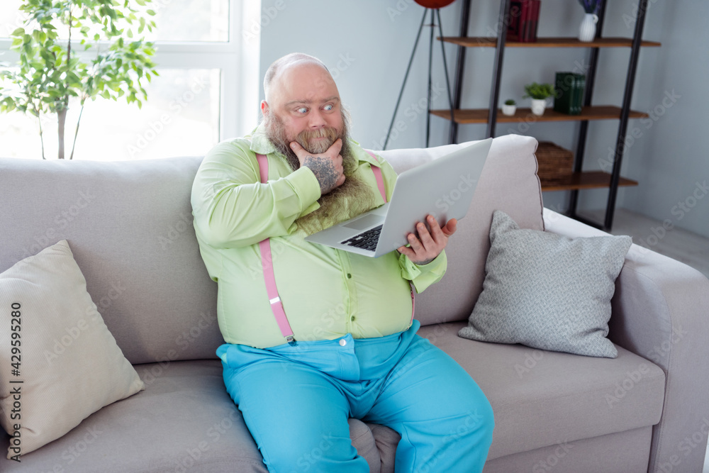 Photo of thoughtful young man sit on couch arm on chin look interested laptop thinking free time indoors Photo of thoughtful young man sit on couch arm on chin look interested laptop thinking free time indoors