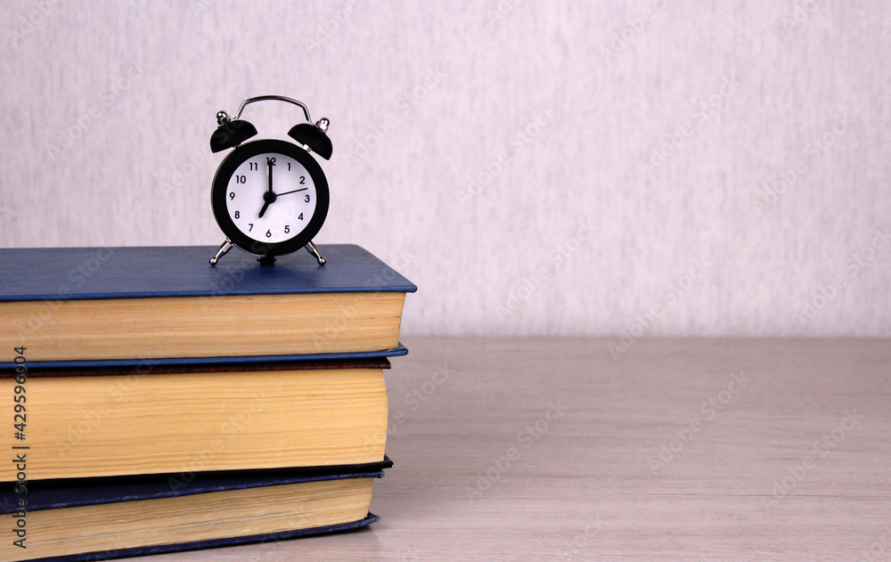 Small black clock on a stack of books on a wooden table Small black clock on a stack of books on a wooden table