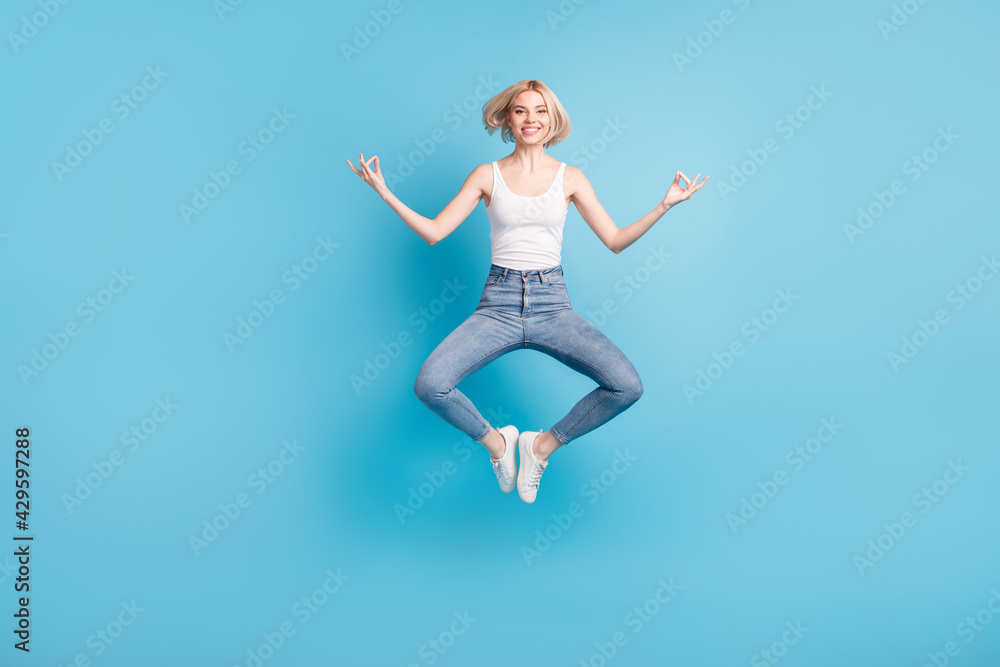 Full length photo of happy charming young woman make om sign yoga jump up isolated on blue color background