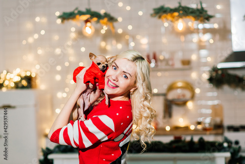 Portrait of a female in dark clothes with a little dog together over light christmas background