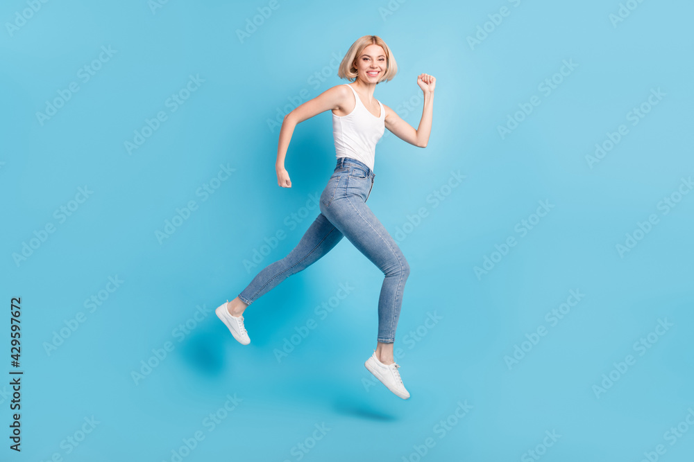 Full size profile side photo of cheerful happy young woman run empty space jump up isolated on blue color background Full size profile side photo of cheerful happy young woman run empty space jump up isolated on blue color background