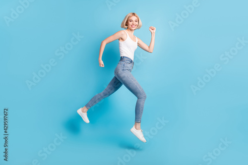 Full size profile side photo of cheerful happy young woman run empty space jump up isolated on blue color background