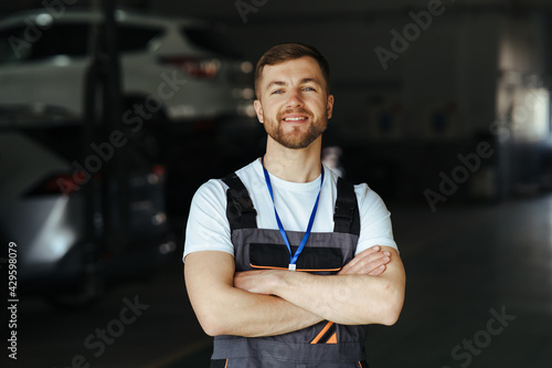 Auto mechanic standing in his workshop in front of a car