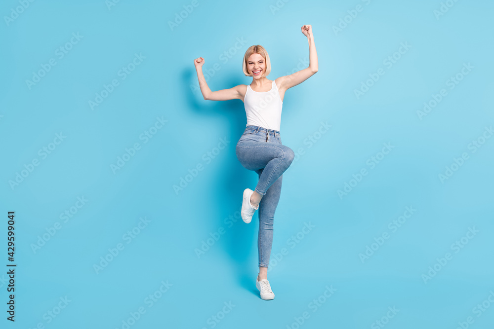 Full length photo of cheerful young woman raise hands winner good mood isolated on blue color background Full length photo of cheerful young woman raise hands winner good mood isolated on blue color background