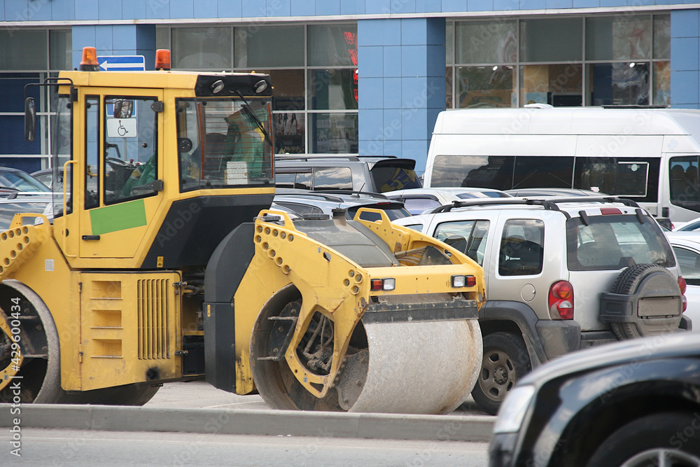 Yellow asphalt road roller in the parking lot for visitors of the shopping center