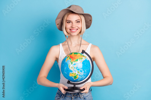 Photo of attractive happy young woman tourist hold hands globe wear hat isolated on blue color background