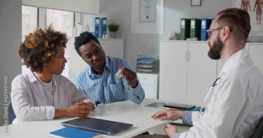 Obraz premium Male doctor giving to young afro-american couple jar of pills.