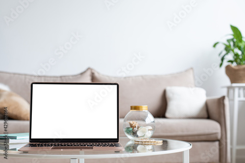 Laptop with blank white screen on the desk, mock up. Personal laptop computer on wood table in living room with modern interior. © uv_group