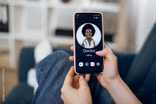 Smartphone app for online medical consultation. Ill female patient holding smartphone, calling young confident African woman doctor via video call program. Distance consultation about treatment.