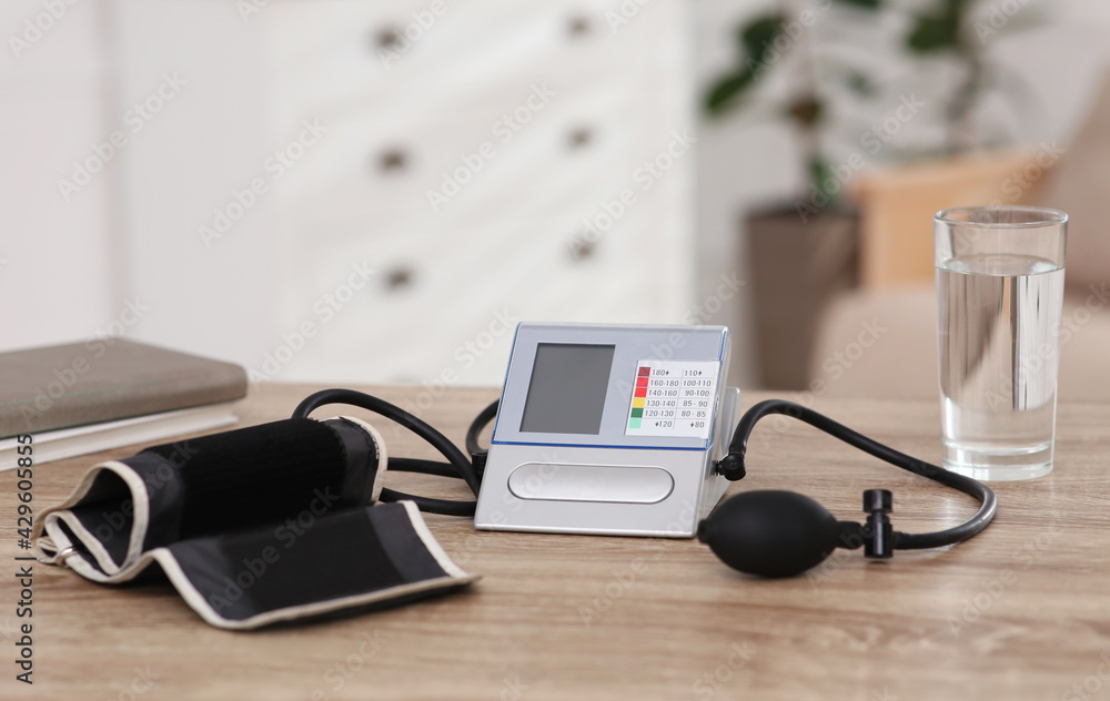 Modern blood pressure monitor and glass of water on wooden table indoors Modern blood pressure monitor and glass of water on wooden table indoors