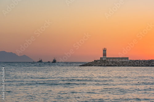Lighthouse and boats in Aegean Sea at dramatical sunset view in Kusadasi, Aydin, Turkey. 